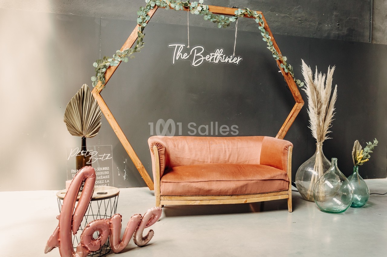 Canapé rose devant un cadre hexagonal en bois décoré de feuillage, avec des vases et des ballons formant le mot ’love’.