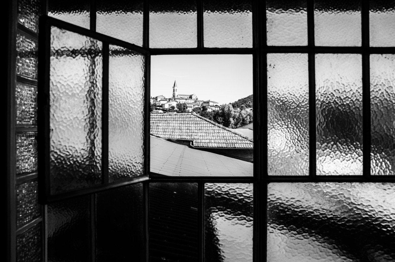 Vue en noir et blanc d'un village avec un clocher, encadrée par une fenêtre à carreaux en verre dépoli.