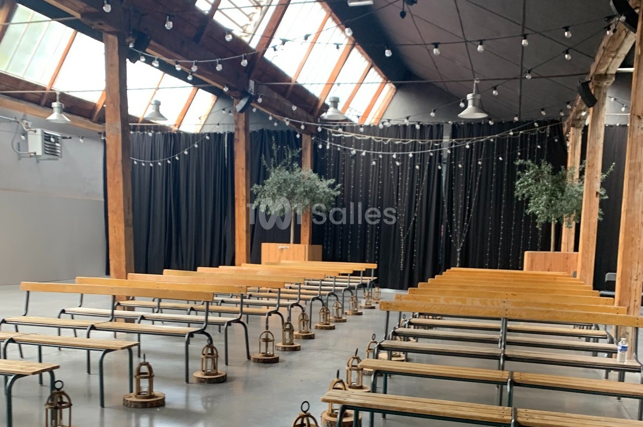 Salle avec des bancs en bois alignés, lanternes au sol, rideaux noirs et guirlandes lumineuses suspendues.