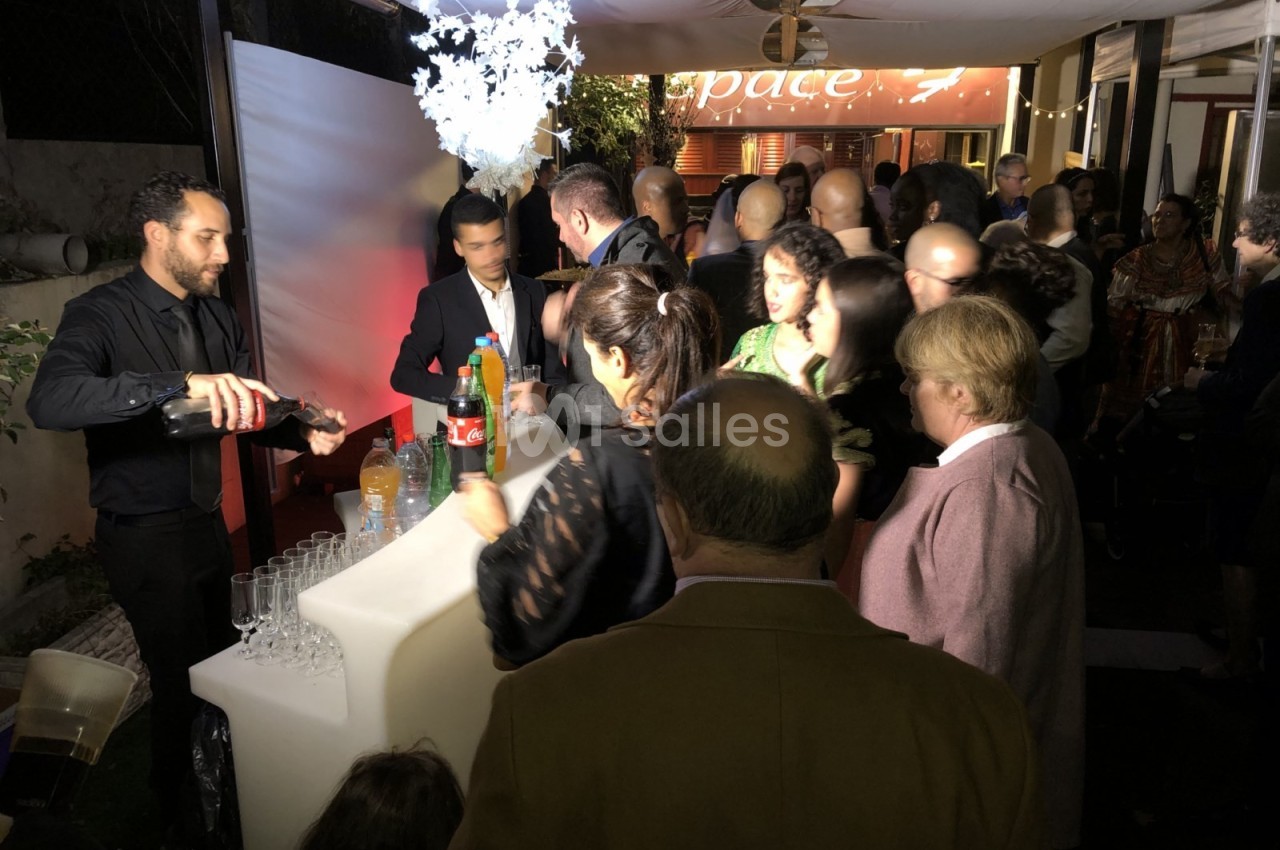 Un barman sert des boissons à un groupe de personnes rassemblées autour d'un comptoir lumineux lors d'un événement en soirée.