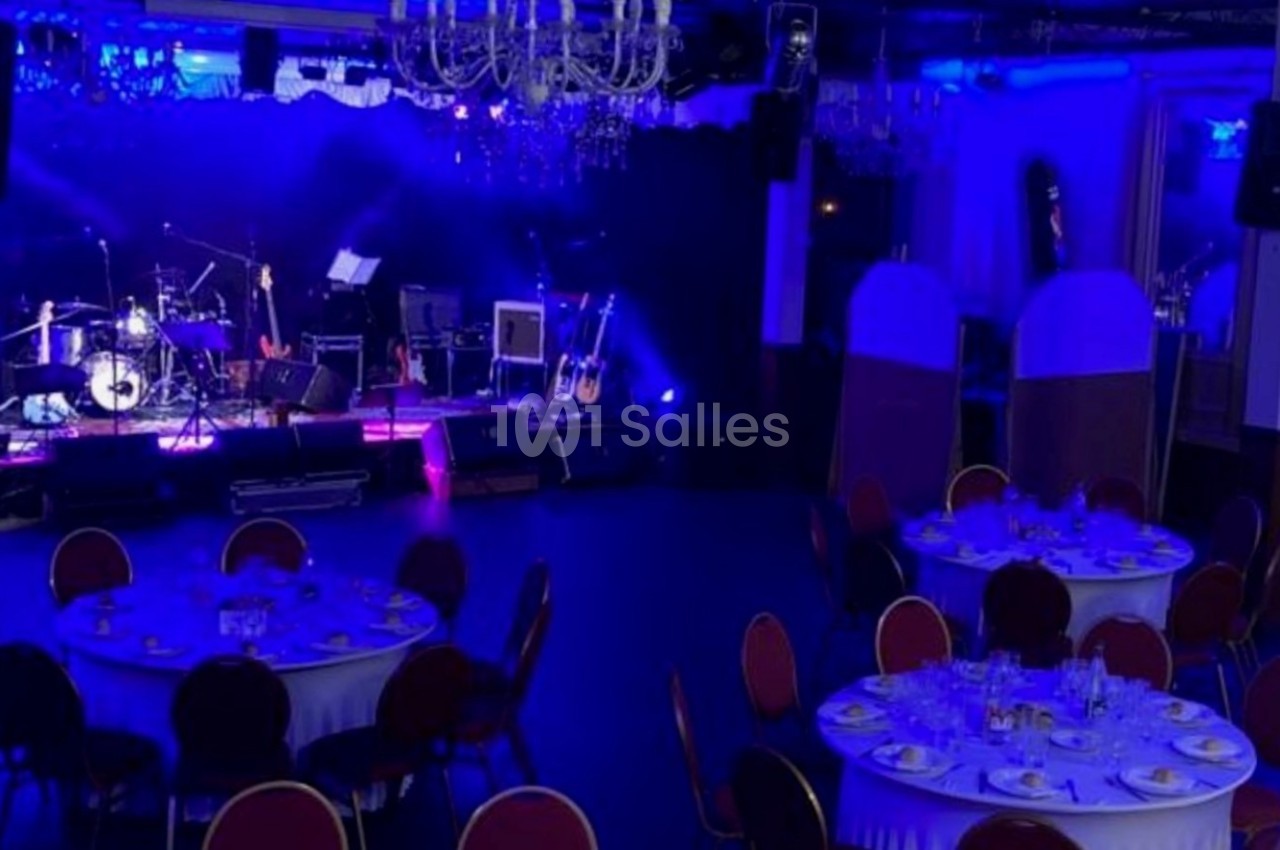 Salle de réception avec tables dressées et une scène équipée d'instruments de musique sous un éclairage bleu.
