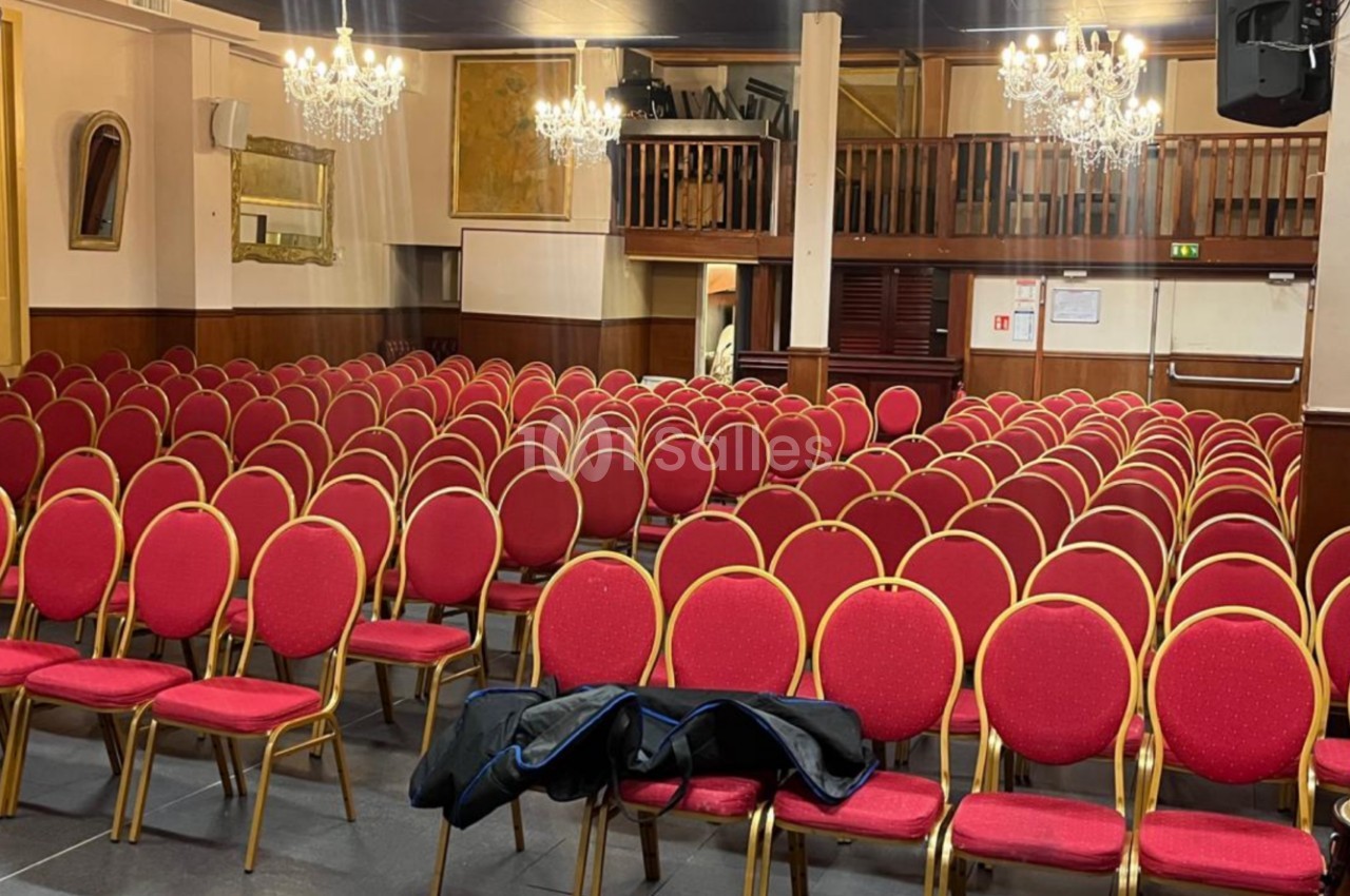 Salle de conférence avec rangées de chaises rouges alignées, lustres suspendus et mezzanine en arrière-plan.