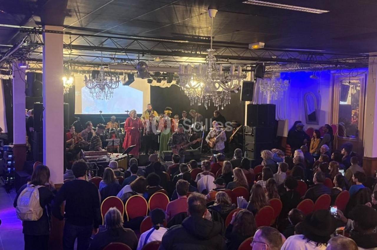 Un groupe de musiciens et chanteurs se produit sur scène devant un public dans une salle éclairée.