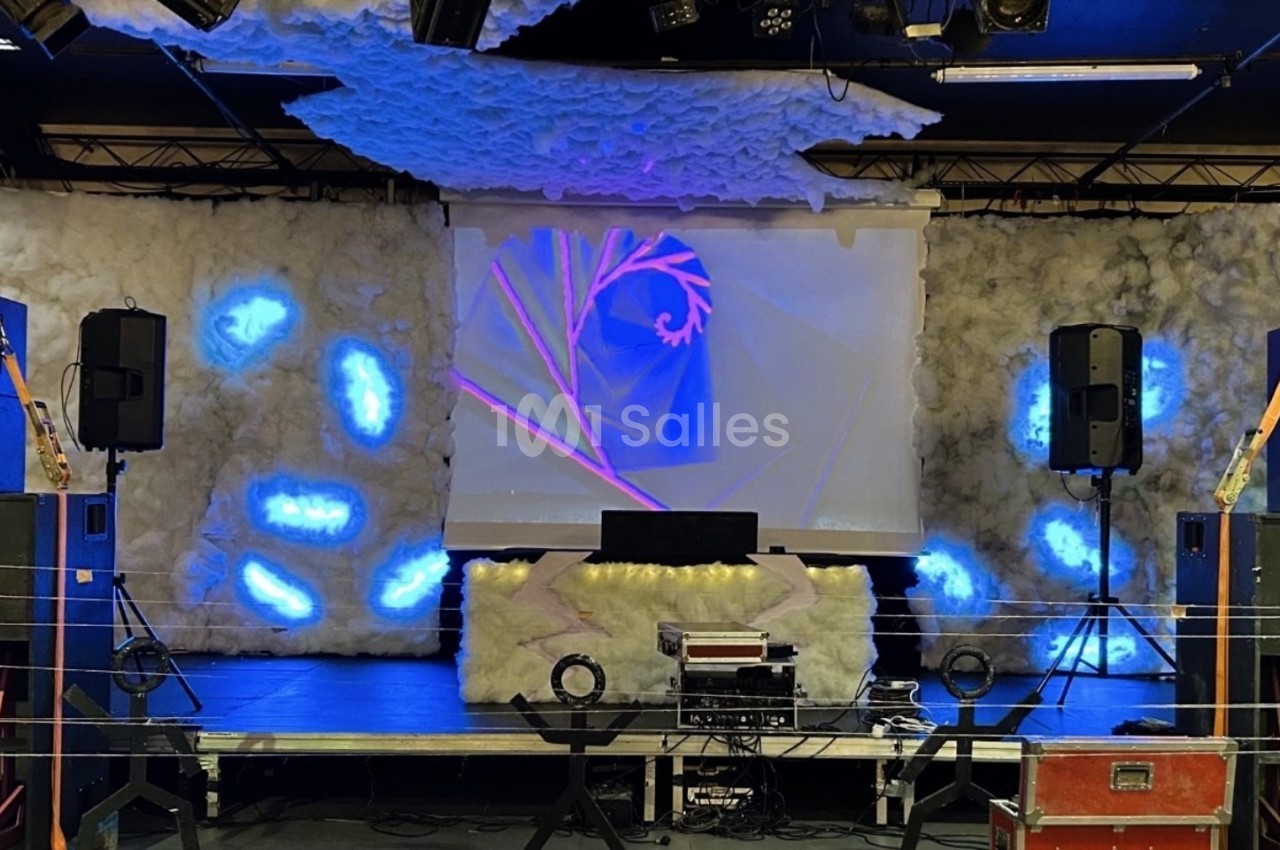 Scène décorée avec des éléments lumineux bleus, un écran projetant des motifs et des équipements audio.