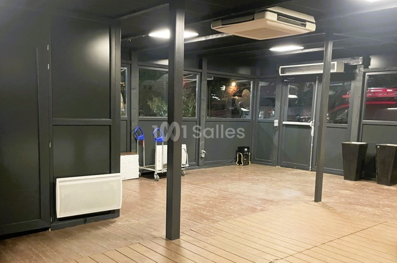 Salle vide avec murs sombres, parquet en bois, climatisation au plafond et fenêtres donnant sur l'extérieur.