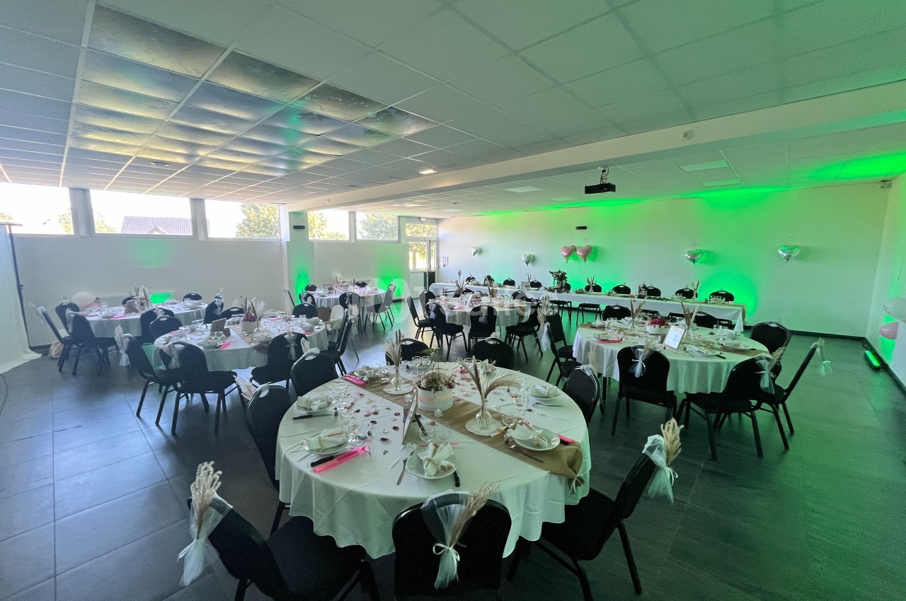 Salle de réception décorée avec des tables rondes dressées, nappes blanches et éclairage d'ambiance vert.