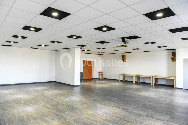 Salle vide avec sol en parquet, murs blancs, plafond à dalles avec éclairage intégré et quelques tables en bois.