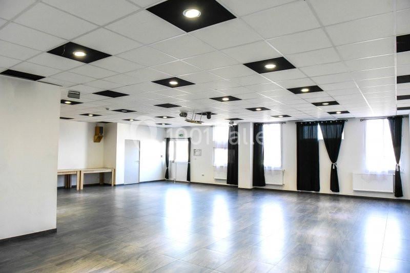 Salle spacieuse avec sol en carrelage, plafond à dalles blanches et éclairage encastré, grandes fenêtres avec rideaux noirs.