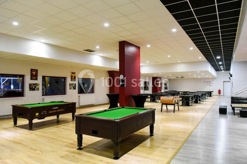 Salle de loisirs avec tables de billard, sol en parquet, murs clairs et éclairage au plafond.