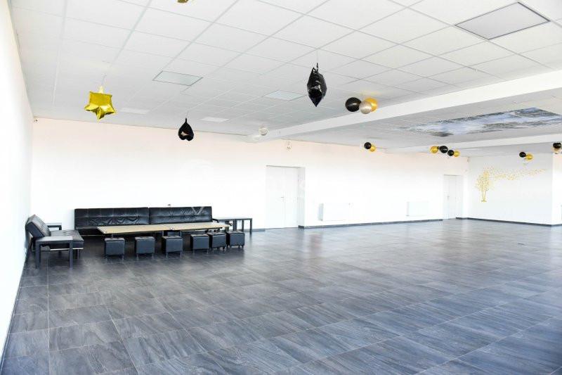 Salle spacieuse avec sol en carrelage gris, plafond blanc et quelques décorations suspendues.