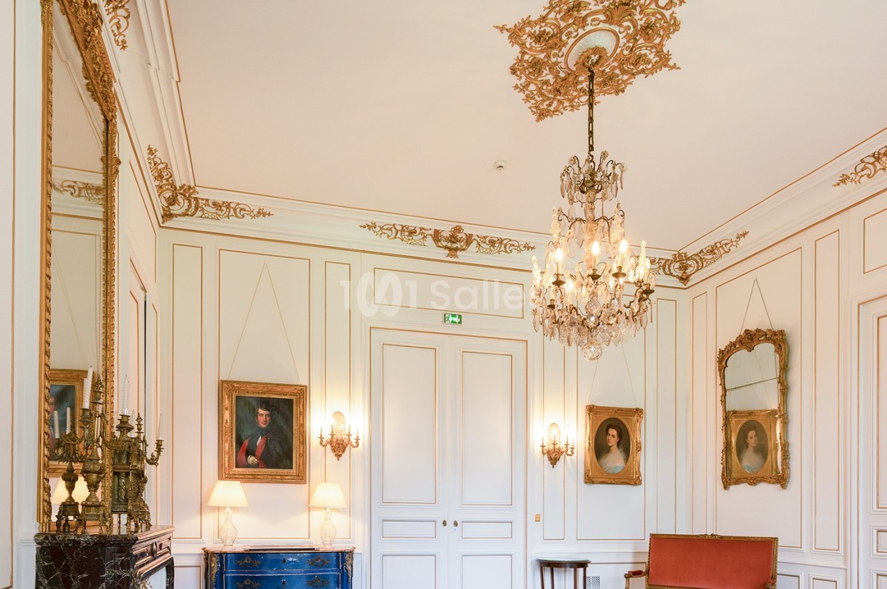 Salon élégant avec moulures dorées, lustre en cristal, portraits encadrés, cheminée en marbre et mobilier classique.