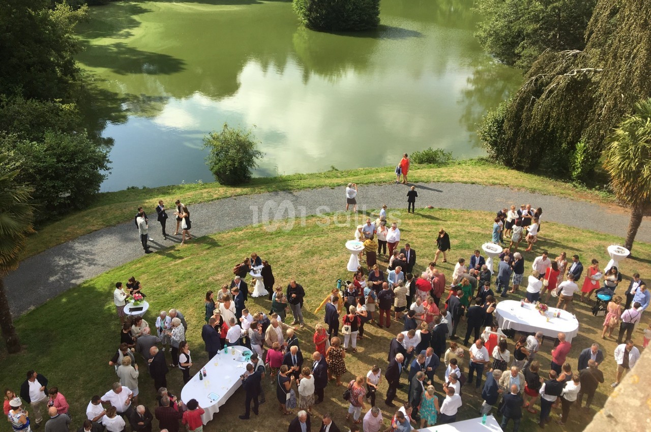 Groupe de personnes rassemblées en plein air près d'un étang, autour de tables hautes, lors d'un événement convivial.