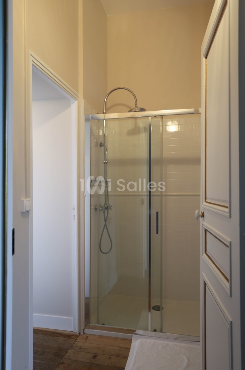 Douche moderne avec paroi vitrée dans une salle de bain aux murs clairs et sol en bois.
