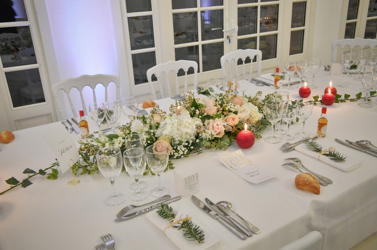 Table élégamment dressée avec une décoration florale centrale, bougies rouges et couverts disposés pour un repas formel.