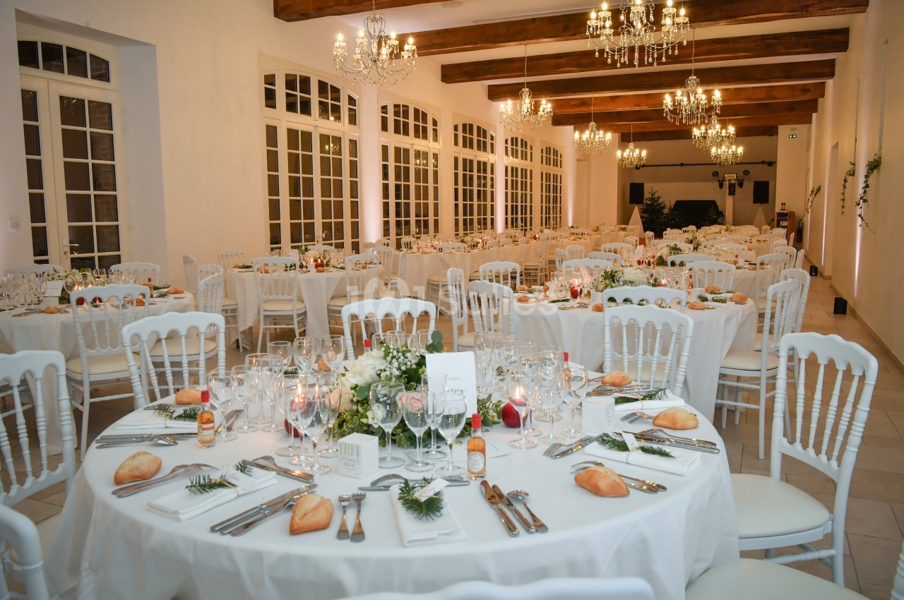 Salle de réception élégante avec tables rondes dressées, décorations florales et chandeliers suspendus.
