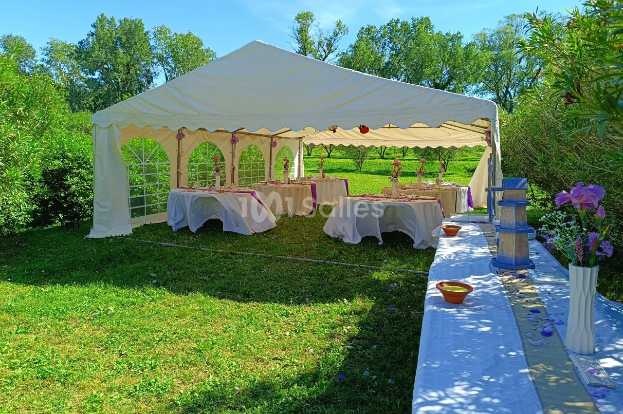 Tente blanche installée dans un jardin verdoyant, avec des tables décorées pour un événement festif en plein air.
