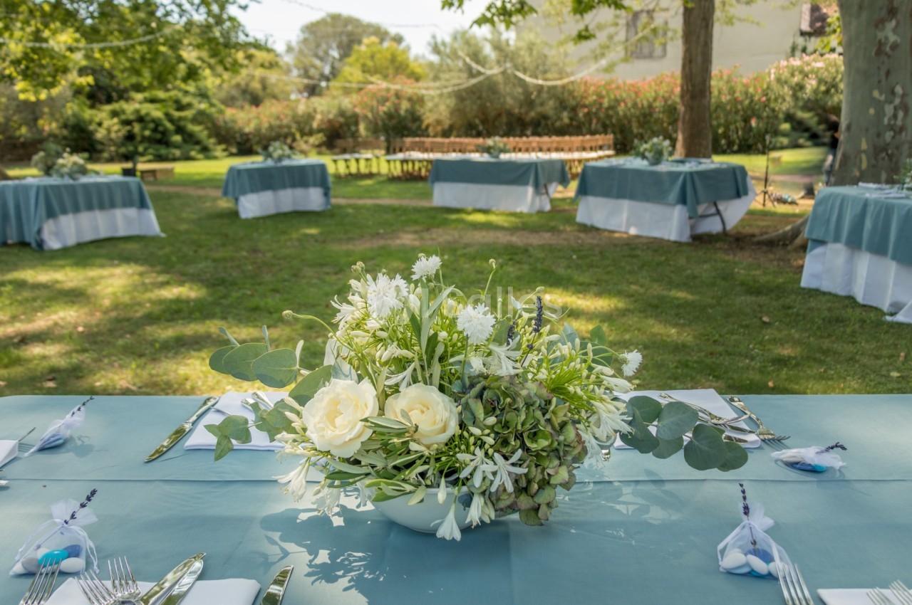 Centre de table floral avec des roses blanches et feuillage, disposé sur une table dressée dans un jardin.