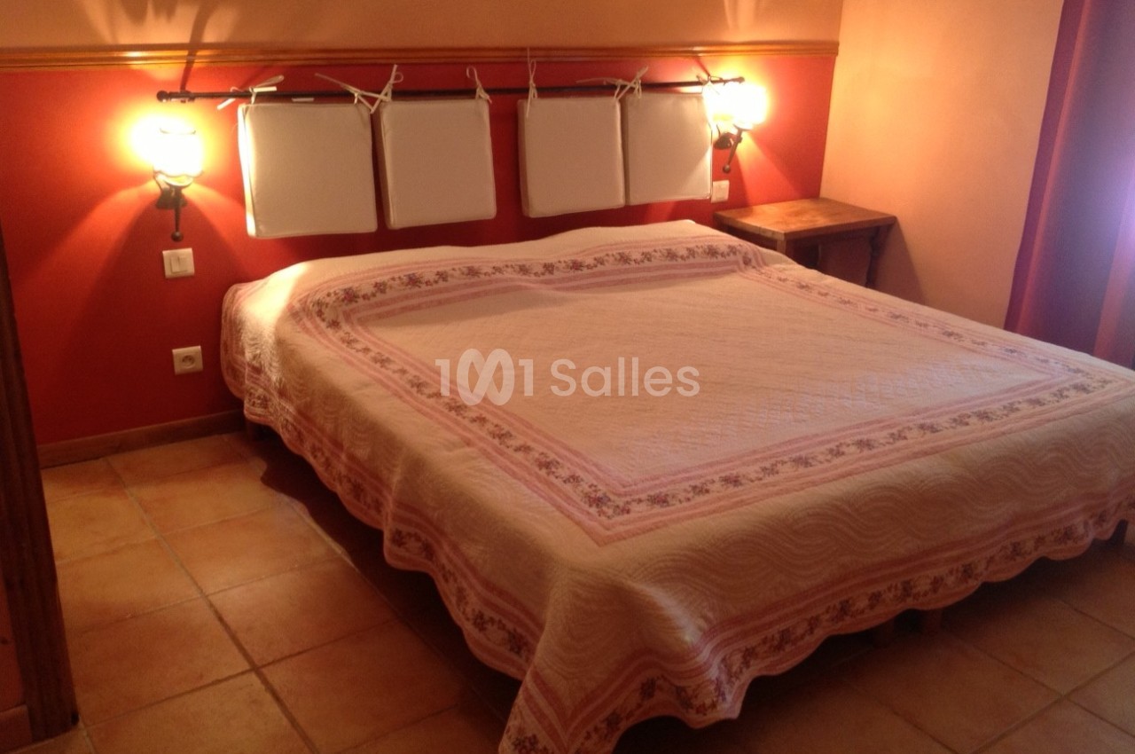 Lit double avec couvre-lit rose et blanc dans une chambre aux murs rouges et orange, éclairée par deux appliques murales.