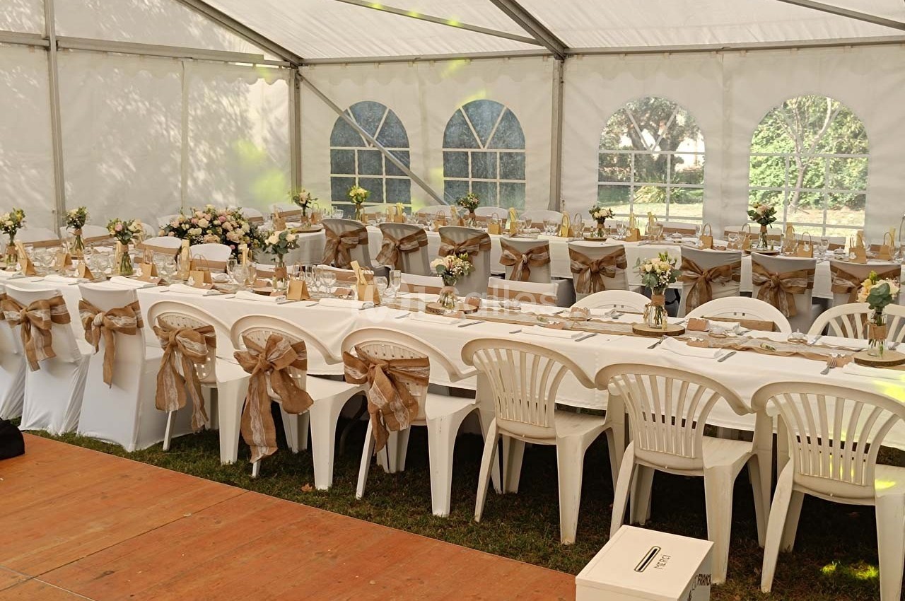 Tables décorées avec nappes blanches, chaises ornées de rubans beiges, disposées sous une grande tente lumineuse.