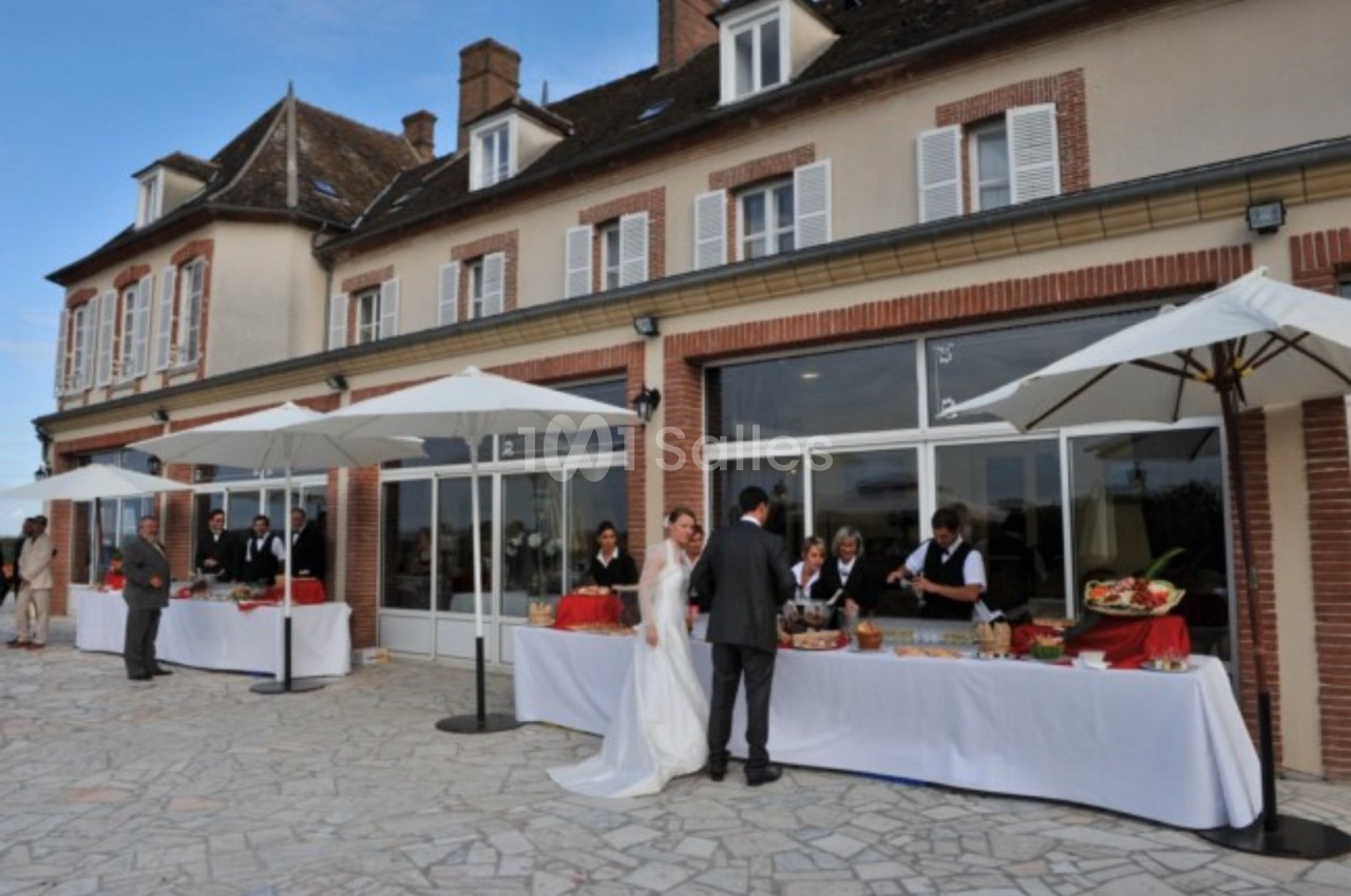 Mariage en extérieur devant une grande maison, avec des buffets sous parasols et des invités en tenue élégante.
