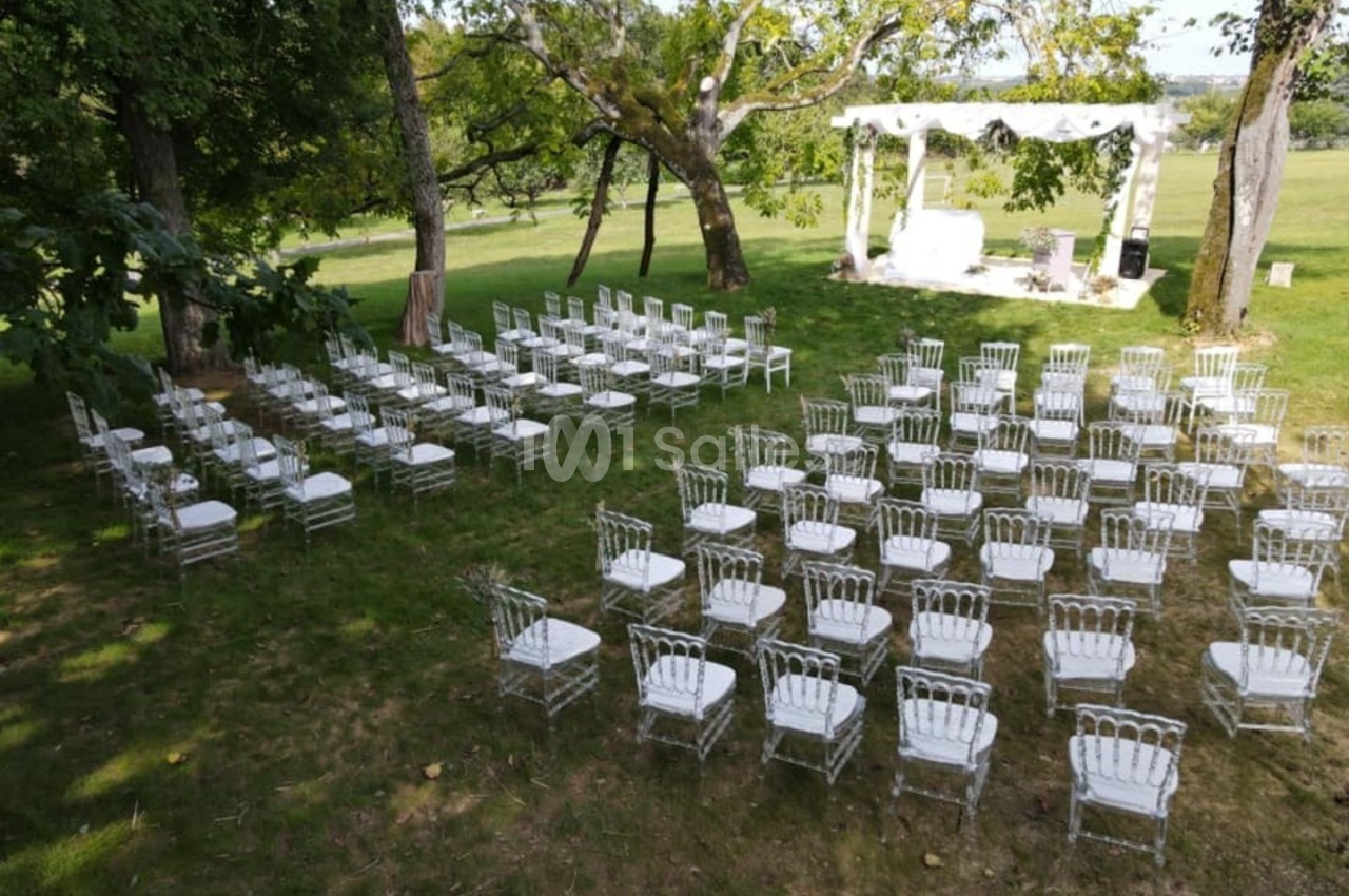 Chaises blanches disposées en rangées sur une pelouse devant une arche décorée pour une cérémonie en plein air.