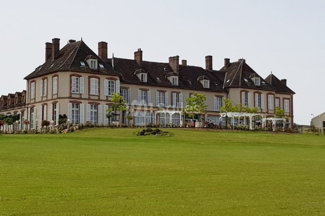 Grand bâtiment de style château entouré de pelouses verdoyantes sous un ciel dégagé.