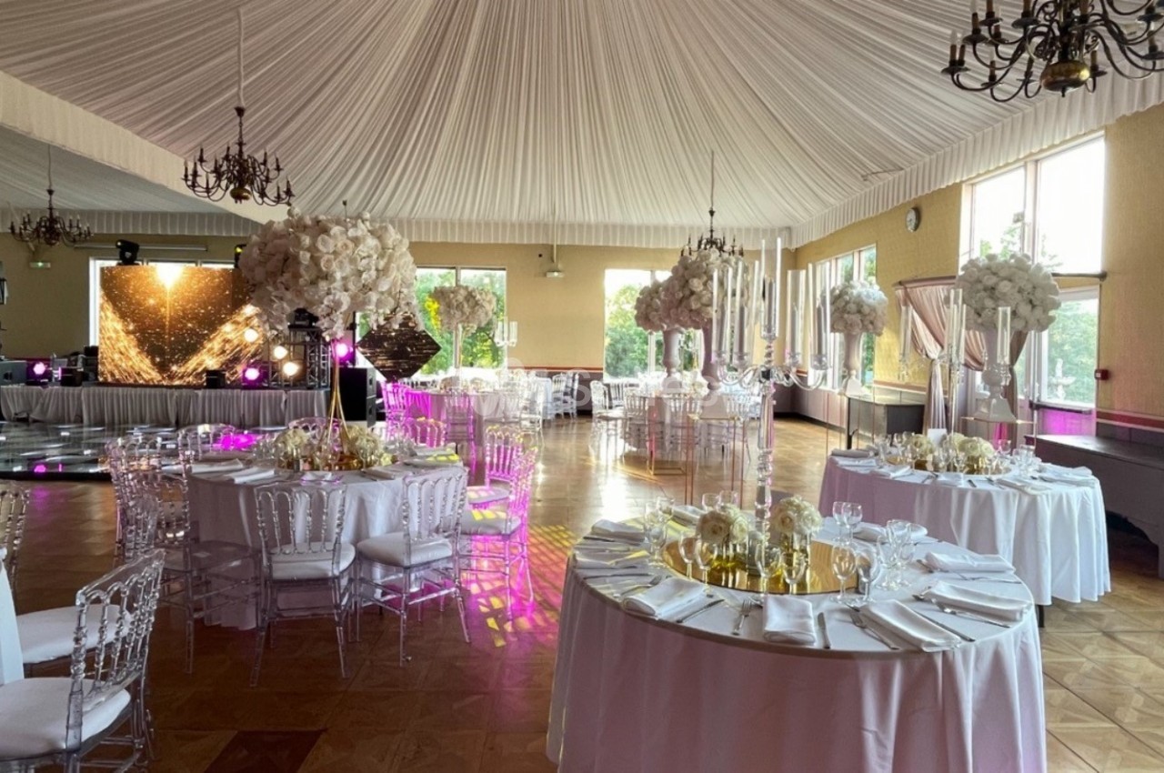 Salle de réception élégante avec tables décorées de fleurs blanches, chaises transparentes et éclairage tamisé.