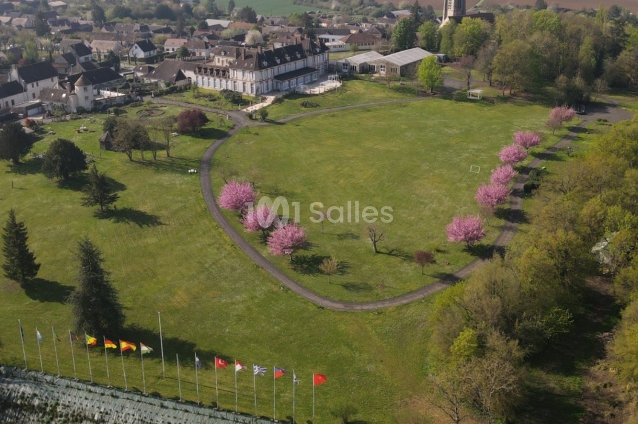 Vue aérienne d'un parc avec pelouse, arbres en fleurs roses, drapeaux alignés et bâtiments résidentiels en arrière-plan.