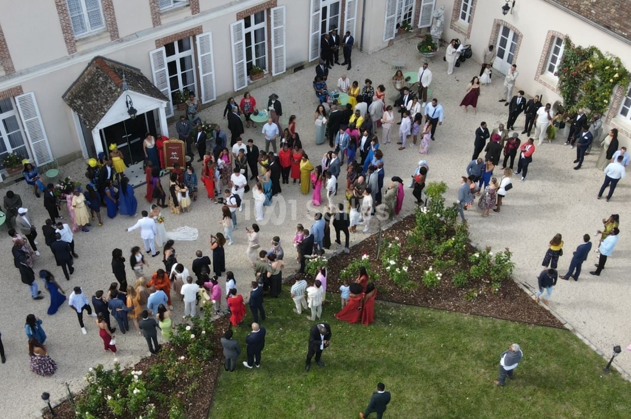 Vue aérienne d'un rassemblement de personnes dans la cour d'un bâtiment avec jardin et parterres de fleurs.