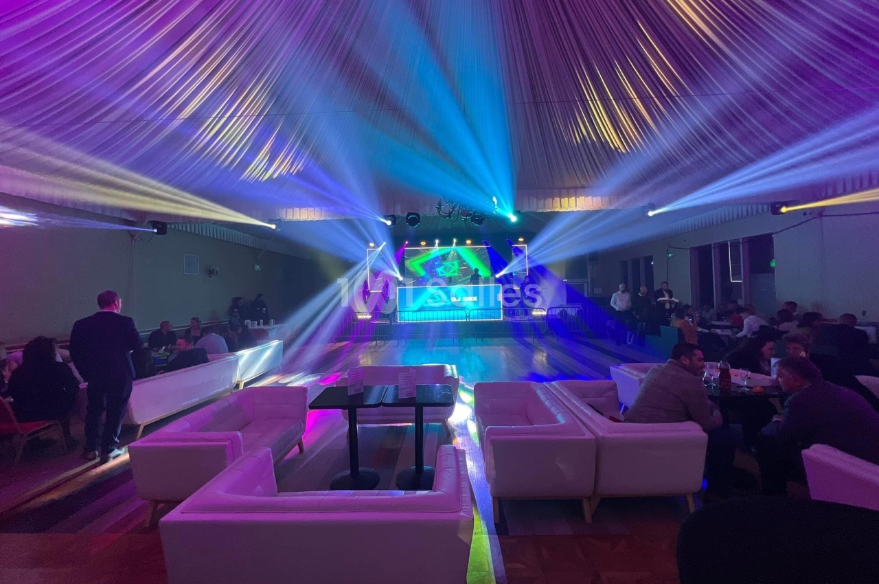 Salle de réception avec éclairage coloré, piste de danse centrale et canapés blancs disposés autour.