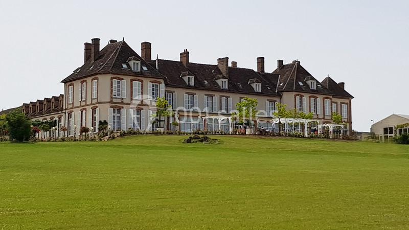 Bâtiment ancien en pierre avec toit en ardoise, grandes fenêtres et terrasse, entouré d'une pelouse verte.