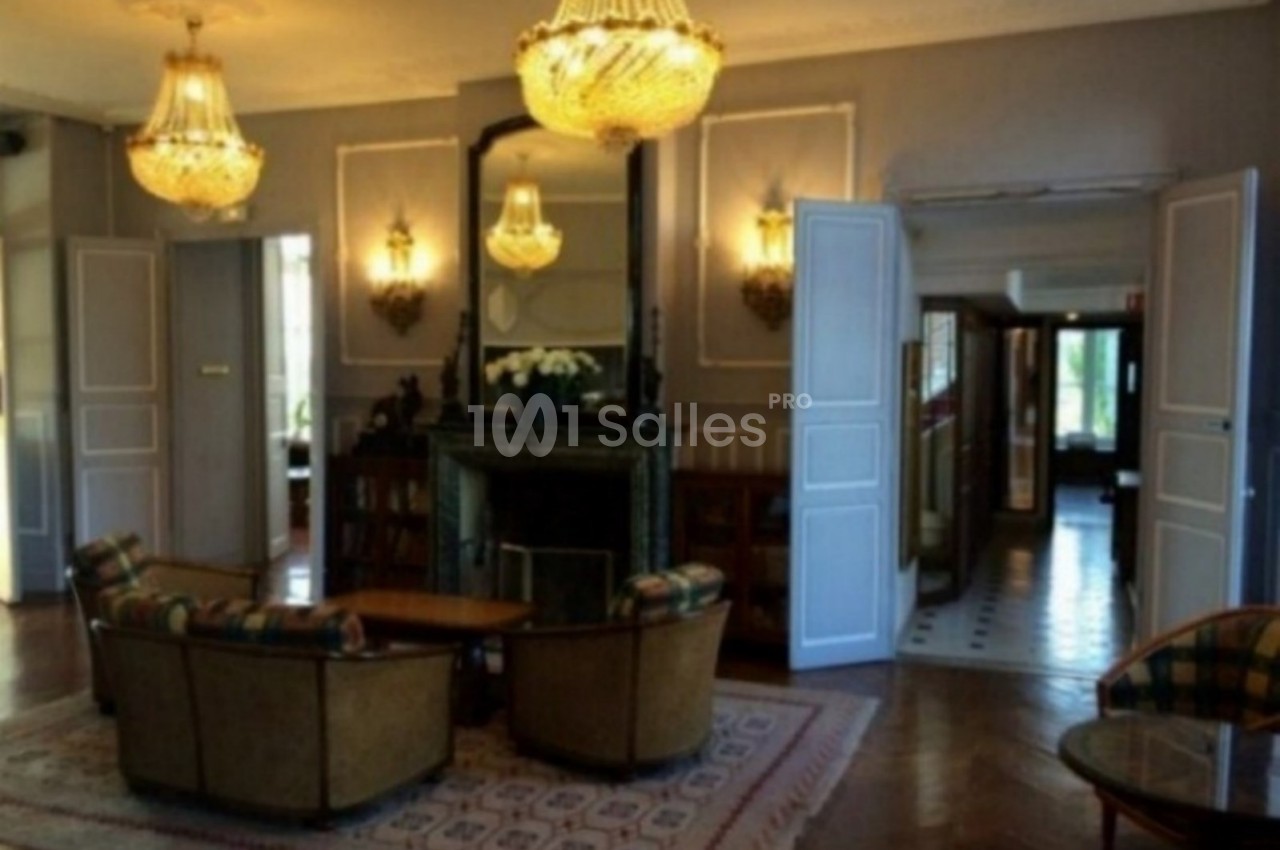 Salon élégant avec cheminée, lustres en cristal, fauteuils autour d'une table basse et parquet en bois.
