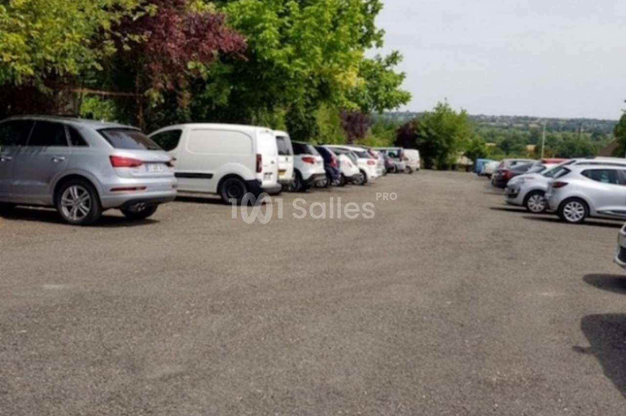 Parking extérieur avec plusieurs voitures stationnées, entouré d'arbres et offrant une vue dégagée sur l'horizon.