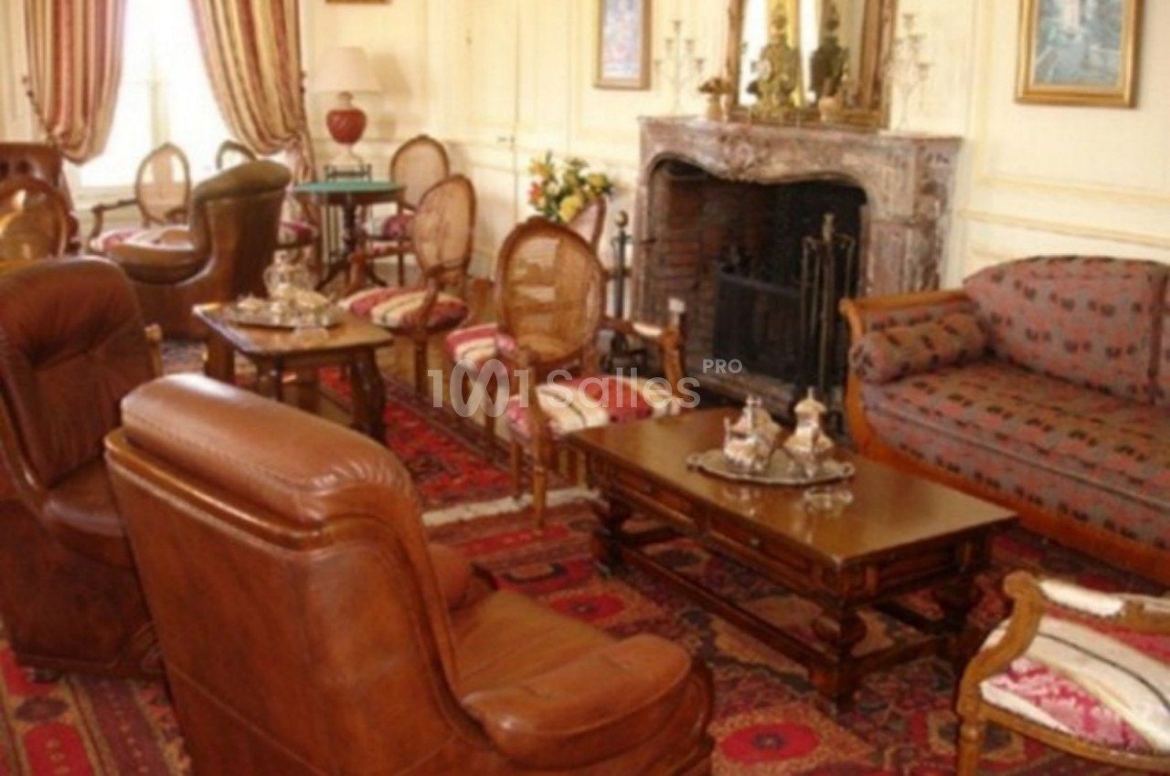 Salon élégant avec mobilier classique, fauteuils en cuir, cheminée en marbre, tapis rouges et décoration raffinée.