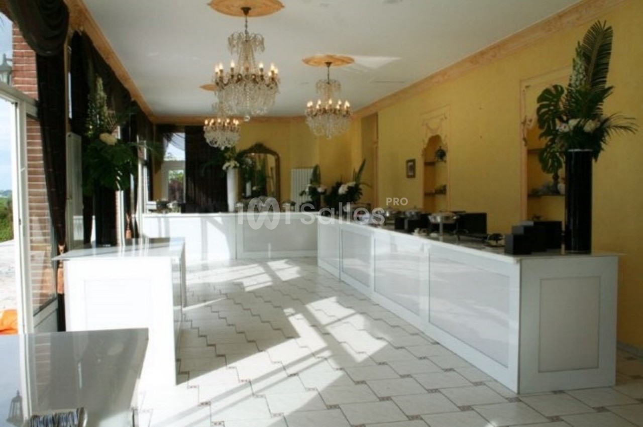 Salle lumineuse avec comptoirs blancs, lustres en cristal, carrelage clair et décorations végétales.