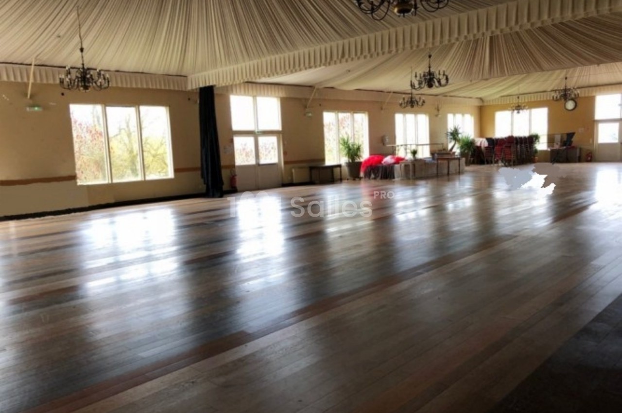 Salle spacieuse avec parquet en bois, plafond drapé et lustres, éclairée par de grandes fenêtres.
