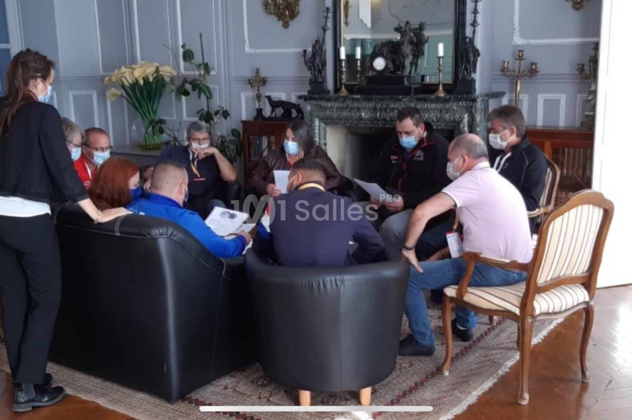 Un groupe de personnes assises en cercle dans un salon, discutant autour de documents, certaines portant un masque.