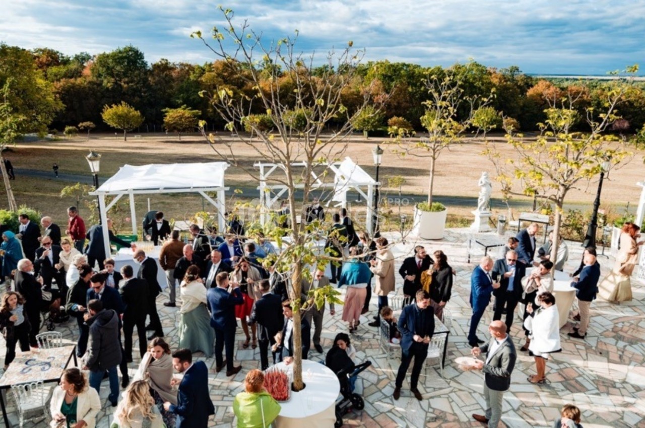 Groupe de personnes rassemblées en extérieur sur une terrasse avec des arbres et des tonnelles, entourée de nature.