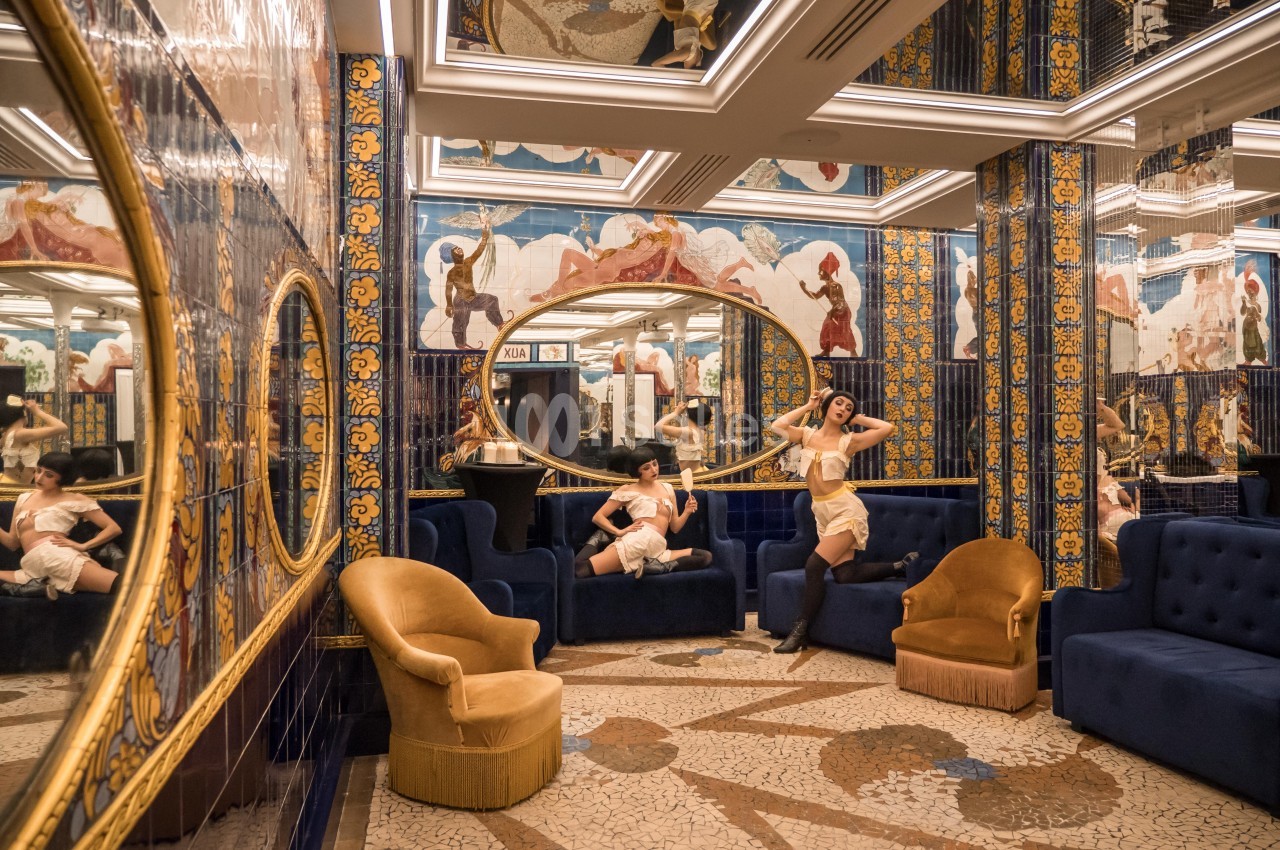 Deux femmes posent dans un salon richement décoré avec des miroirs, des mosaïques et des fresques colorées.