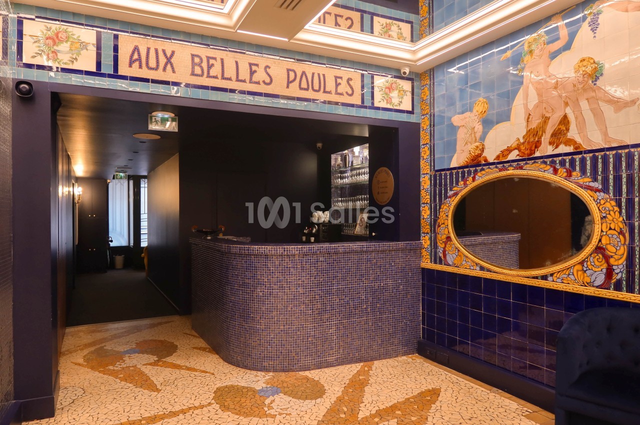 Accueil d'un établissement décoré de mosaïques bleues et de fresques murales, avec un comptoir arrondi en carrelage.
