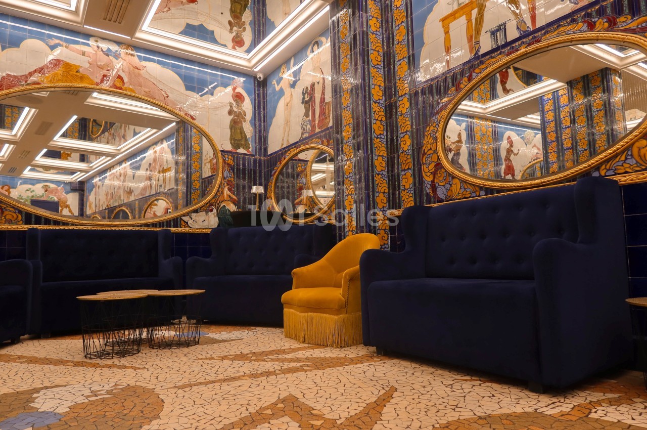 Salon décoré de mosaïques colorées, miroirs ovales dorés, fauteuils bleus et un fauteuil jaune central.