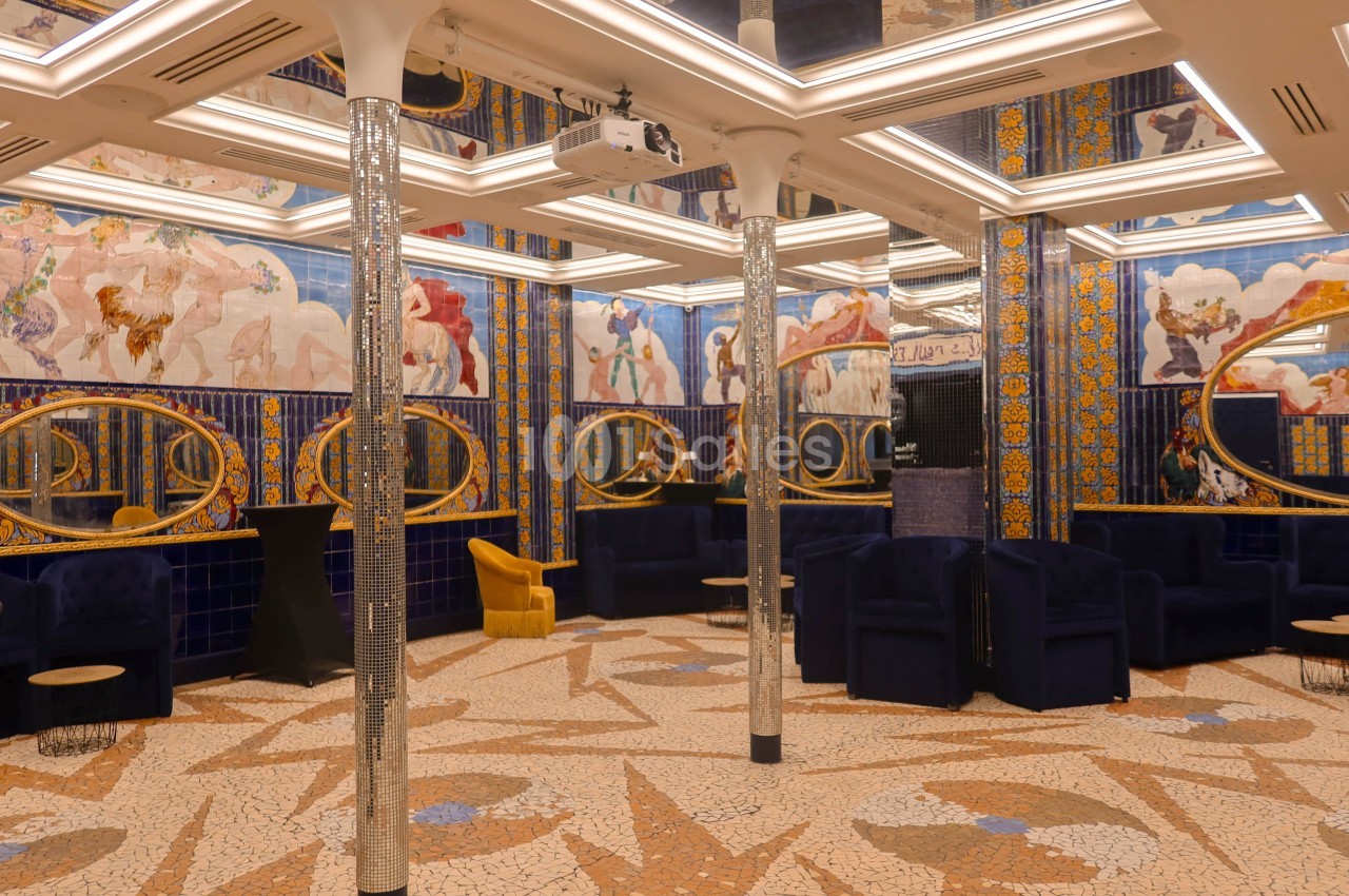 Salle décorée avec des mosaïques au sol, fresques murales colorées, miroirs ovales et mobilier bleu et doré.
