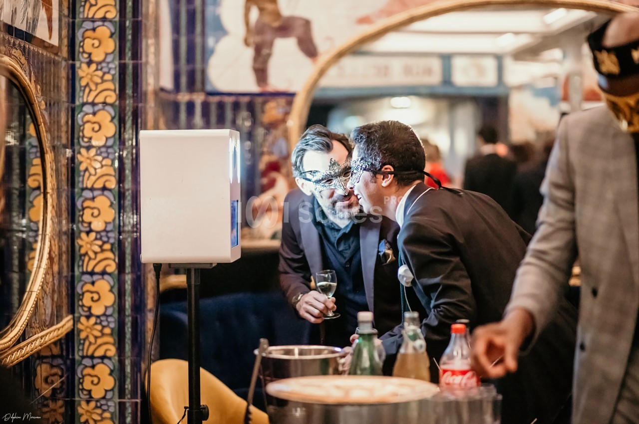 Deux hommes discutent près d'une table avec des boissons, dans un espace décoré de miroirs et de carreaux colorés.