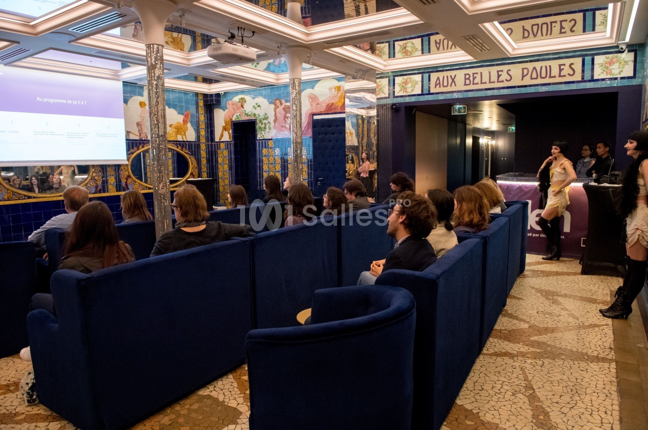 Personnes assises dans une salle colorée avec des fresques murales, regardant une présentation projetée sur un écran.