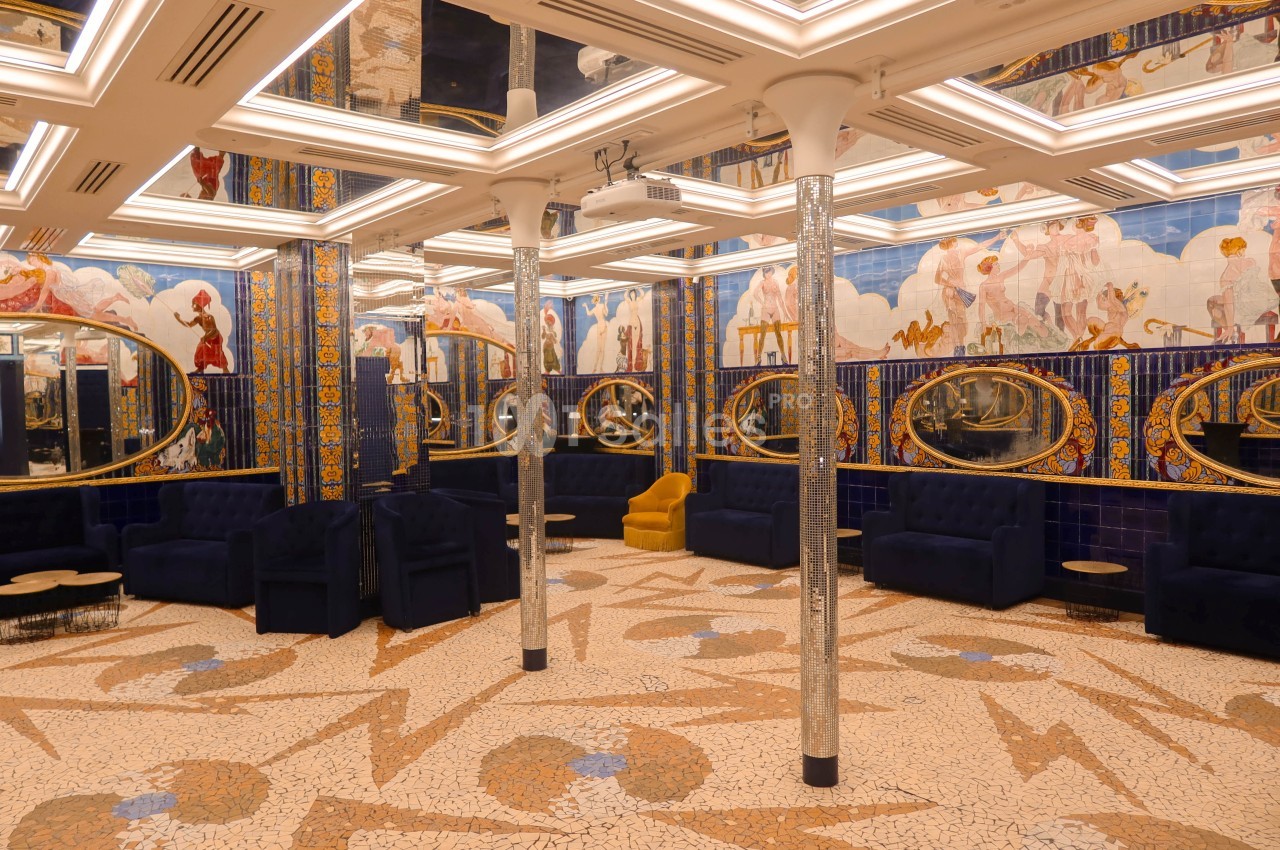 Salle ornée de mosaïques colorées, fresques murales et miroirs ovales, avec des fauteuils bleus et jaunes.
