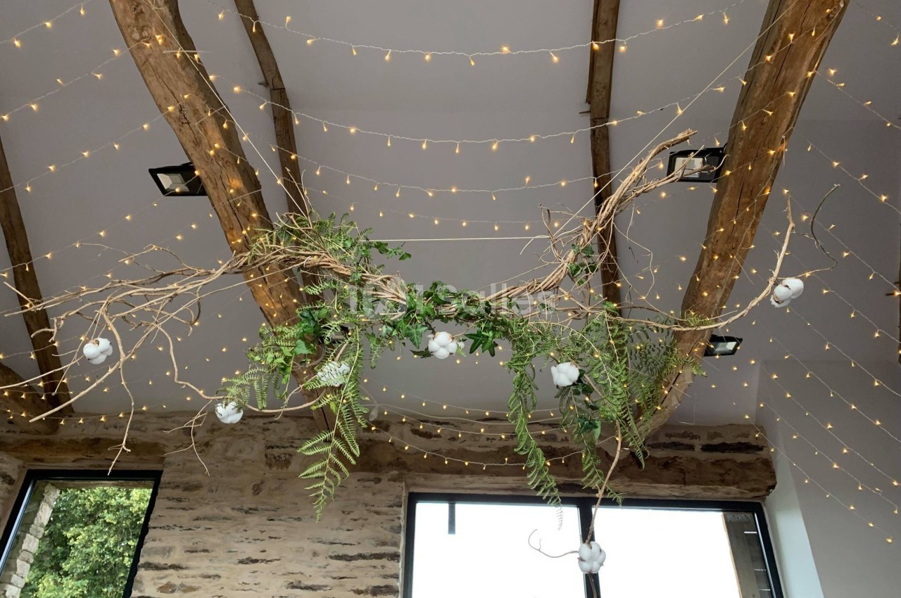 Guirlandes lumineuses suspendues à des poutres en bois avec des branches décoratives et feuillages verts.