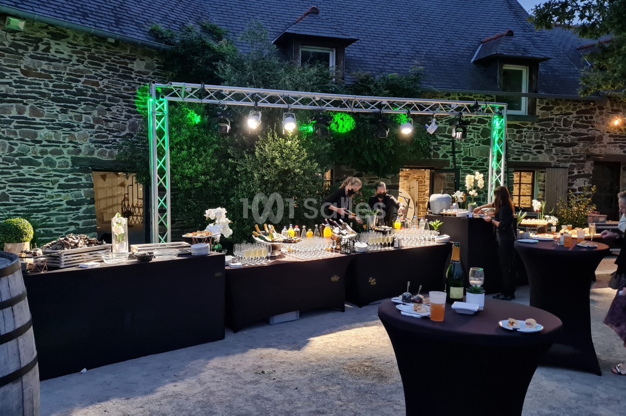 Buffet en extérieur avec tables hautes, éclairage nocturne et invités se servant dans un cadre en pierre.