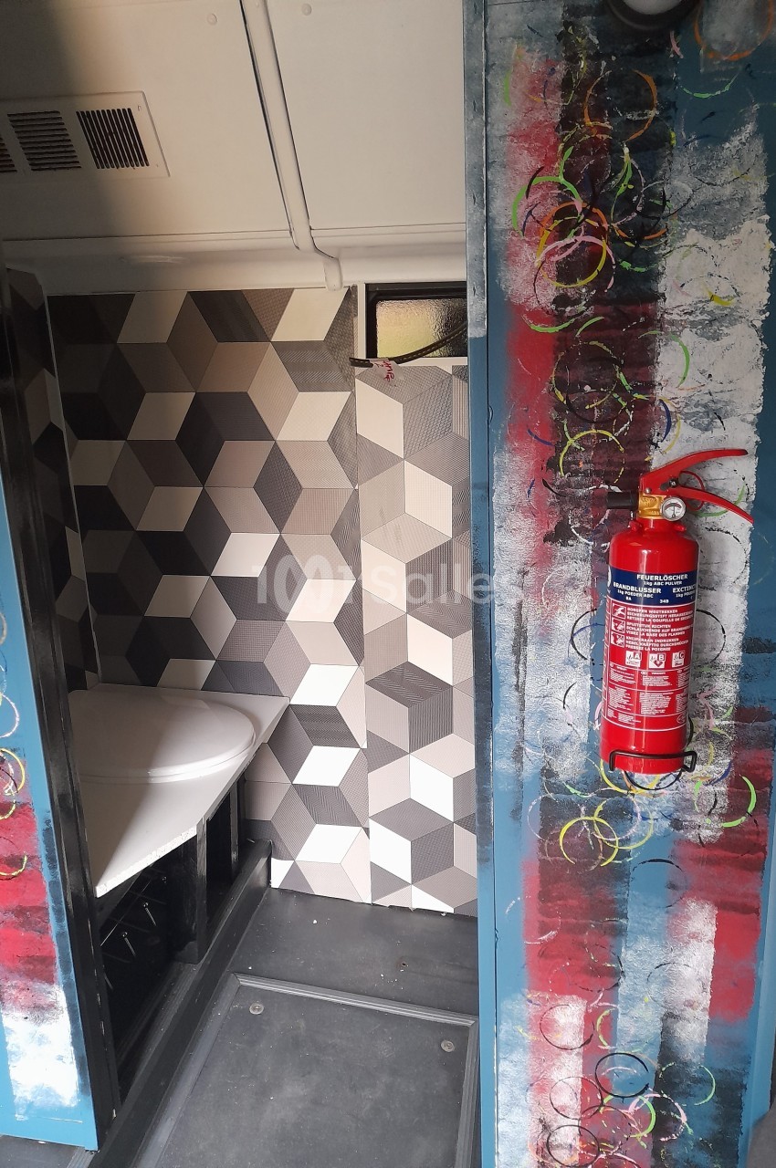 Intérieur d'un espace avec un mur en carreaux géométriques, un extincteur rouge fixé et des décorations colorées.