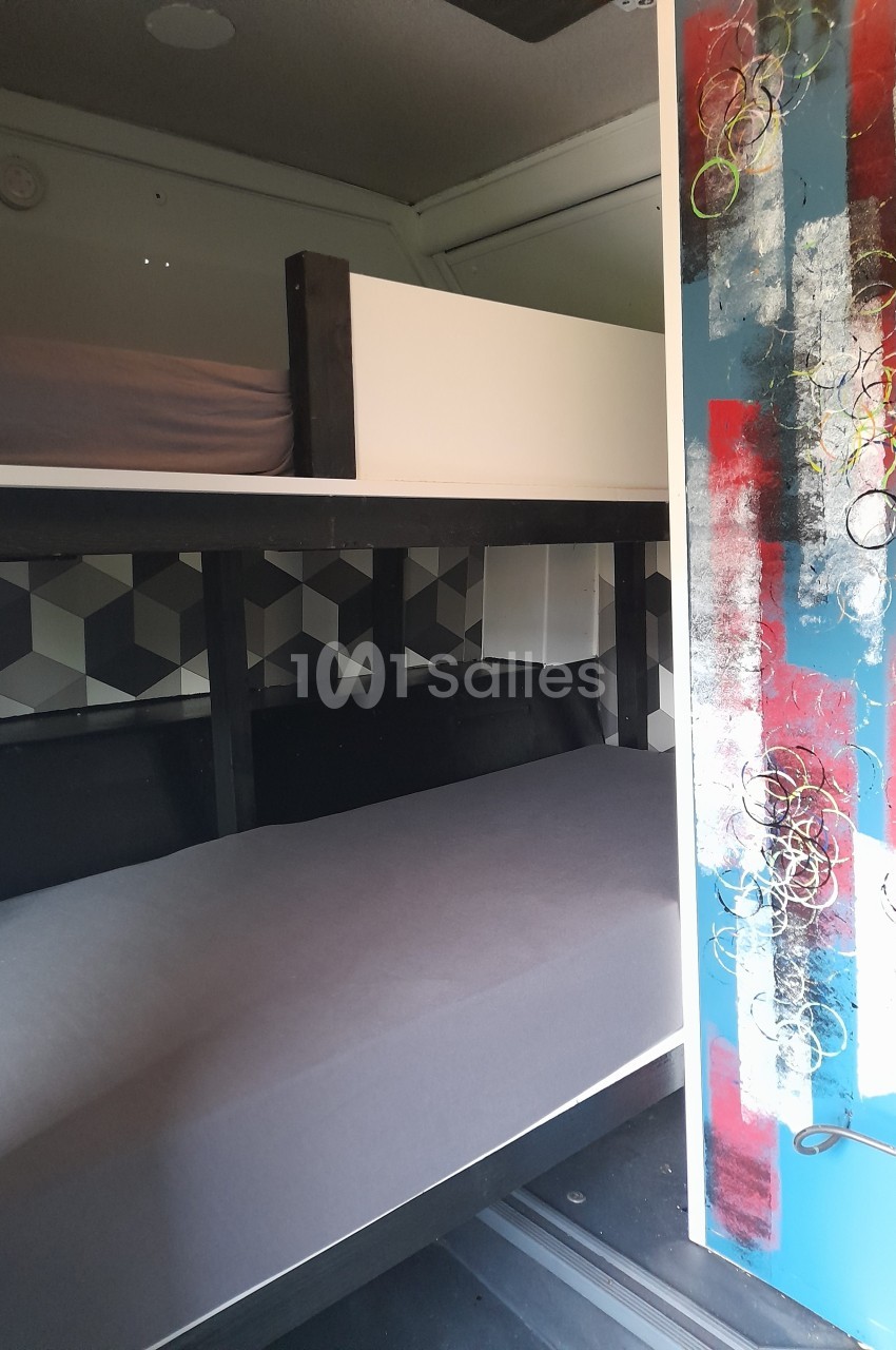 L'intérieur d'un véhicule aménagé avec deux lits superposés et une porte décorée de motifs colorés.