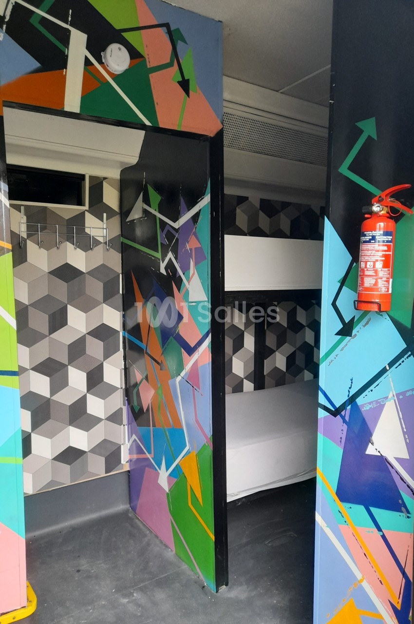Porte colorée ouverte sur une petite chambre avec lits superposés et murs au motif géométrique.